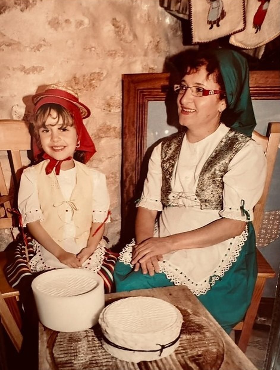 Mujer y niña con traje tradicional junto a quesos de El Gorrión